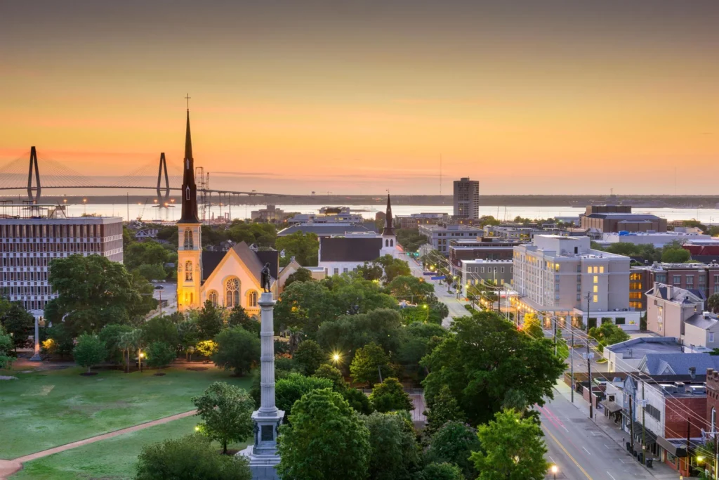 A picturesque sunset in Charleston, SC, with the cityscape illuminated; an immigration lawyer's office is in view.