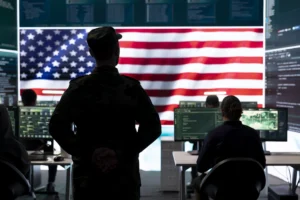 A uniformed officer oversees analysts in a high-tech command center beneath a massive American flag, reminiscent of “ICE Palantir ImmigrationOS.”
