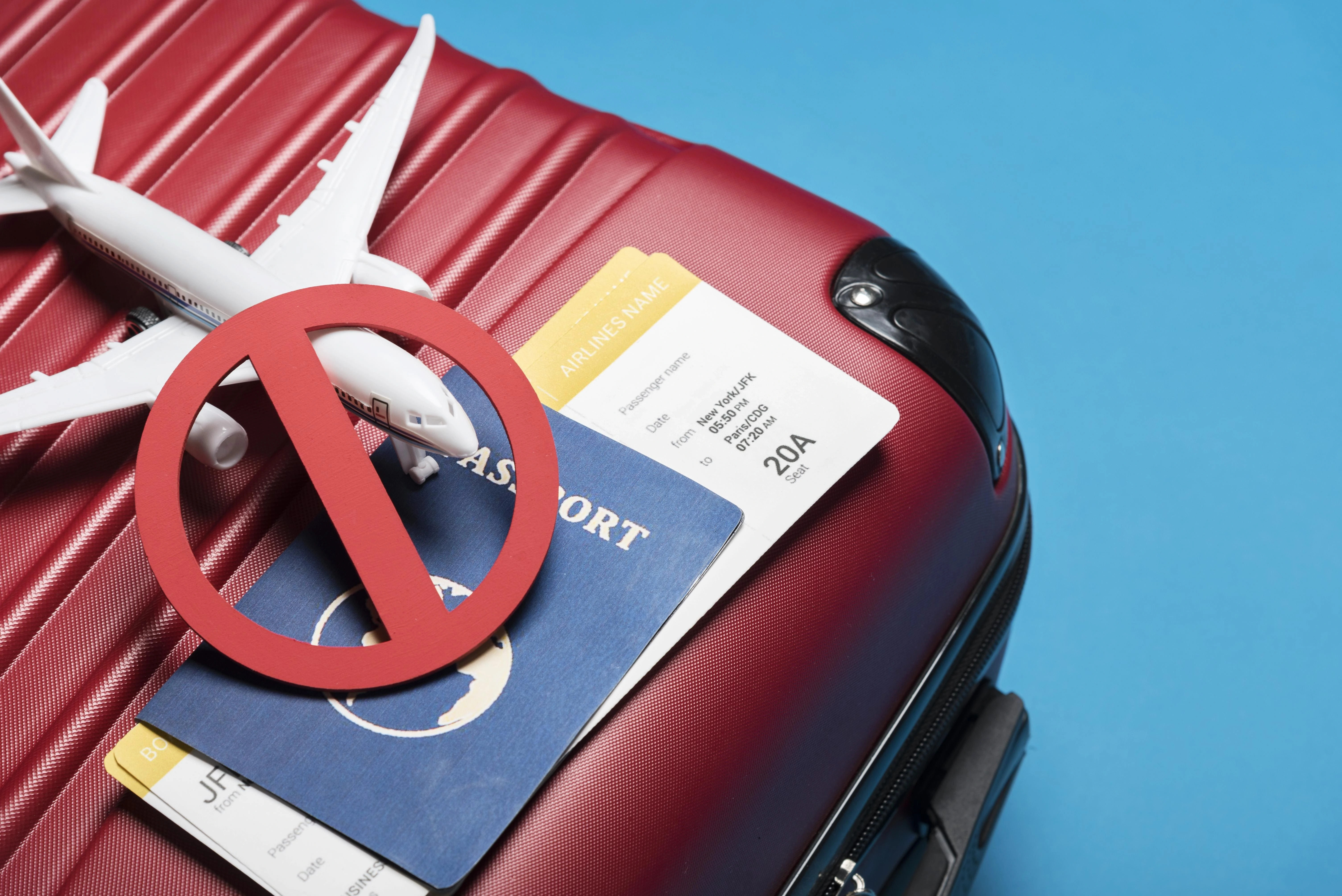 Airline ticket, passport, and red suitcase displayed, indicating travel readiness amidst the US Visa Revocation Rules Update.