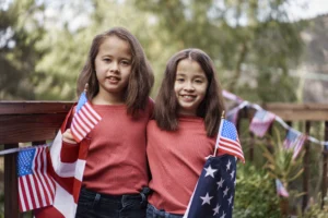 Two young girls with American flags, representing unity and the importance of immigrant rights in California and New York. Special Immigrant Juvenile Status in 2026