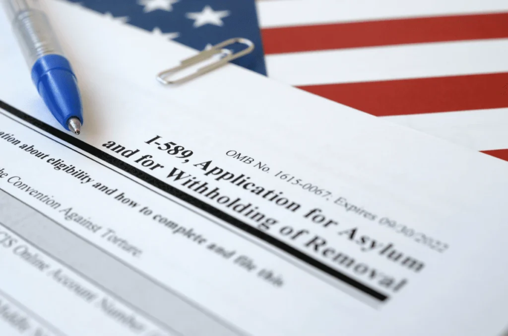 Formulario I-589 de solicitud de asilo y suspensión de deportación en Estados Unidos sobre una bandera estadounidense, representando el proceso de asilo e inmigración en 2026.