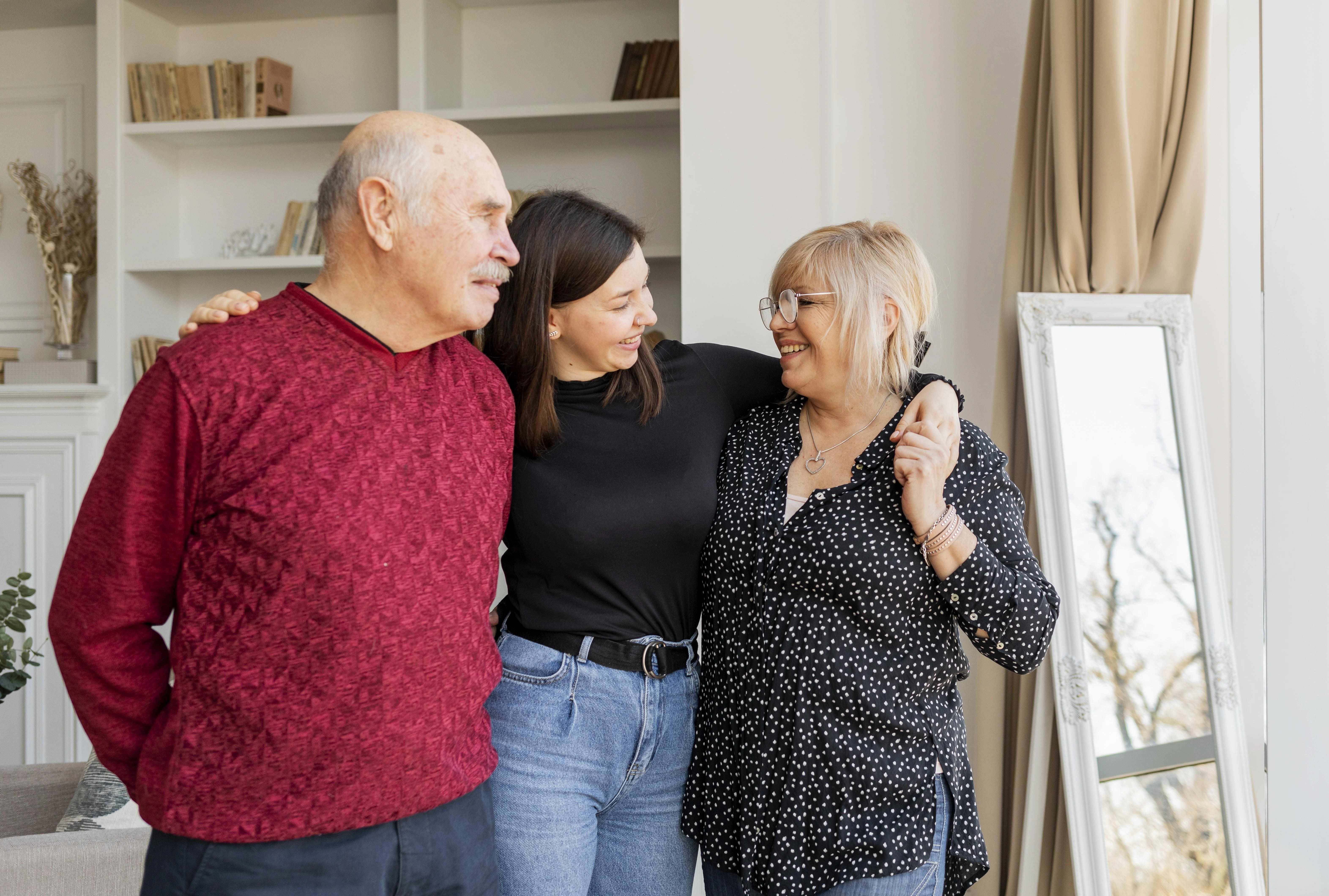 Adult daughter with her arms around her elderly parents at home, representing a U.S. citizen sponsoring parents for an IR-5 green card