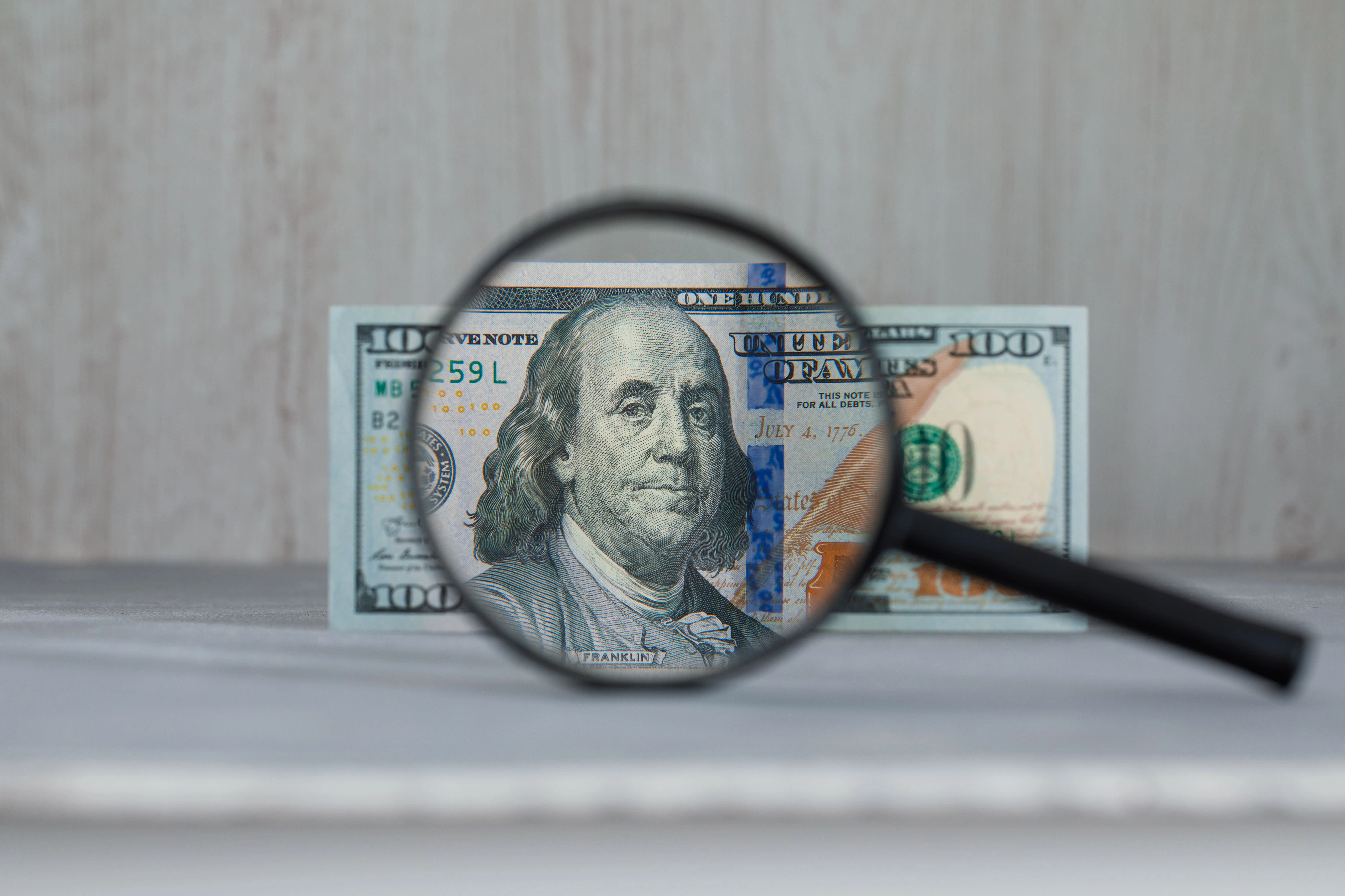 Magnifying glass over a U.S. dollar bill, symbolizing the H-1B prevailing wage used to determine the minimum salary for an LCA.