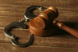 Un mazo de juez de madera y un par de esposas metálicas abiertas sobre una mesa de madera, representando la diferencia legal entre estar detenido y arrestado.