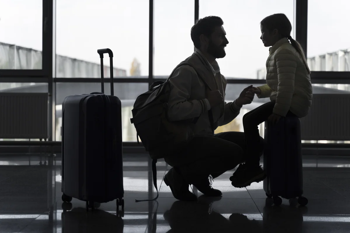 A father and daughter at an airport, holding hands beside their luggage, symbolizing the journey through the asylum process. Learn how the asylum process works with Aftalion Law Group.