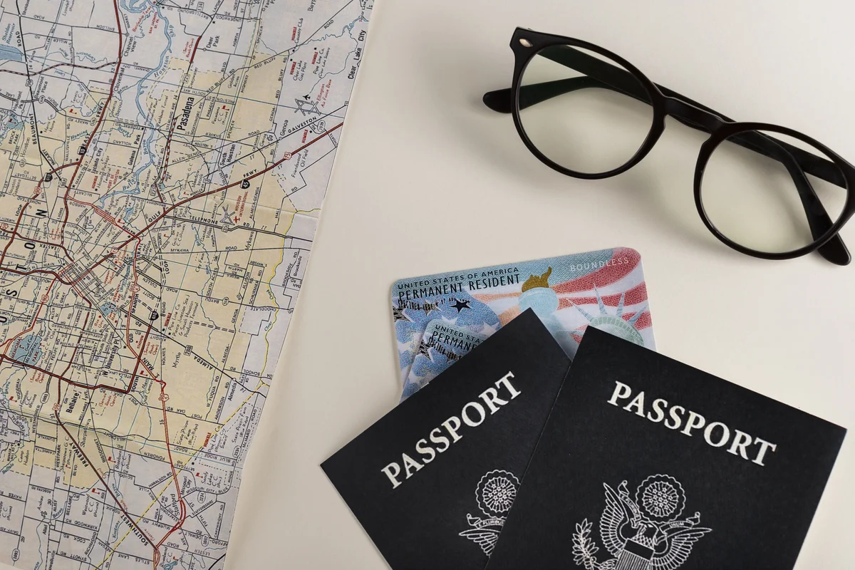 Passports, a green card, a map, and glasses on a desk, symbolizing preparation for family-based visa interview questions in California.