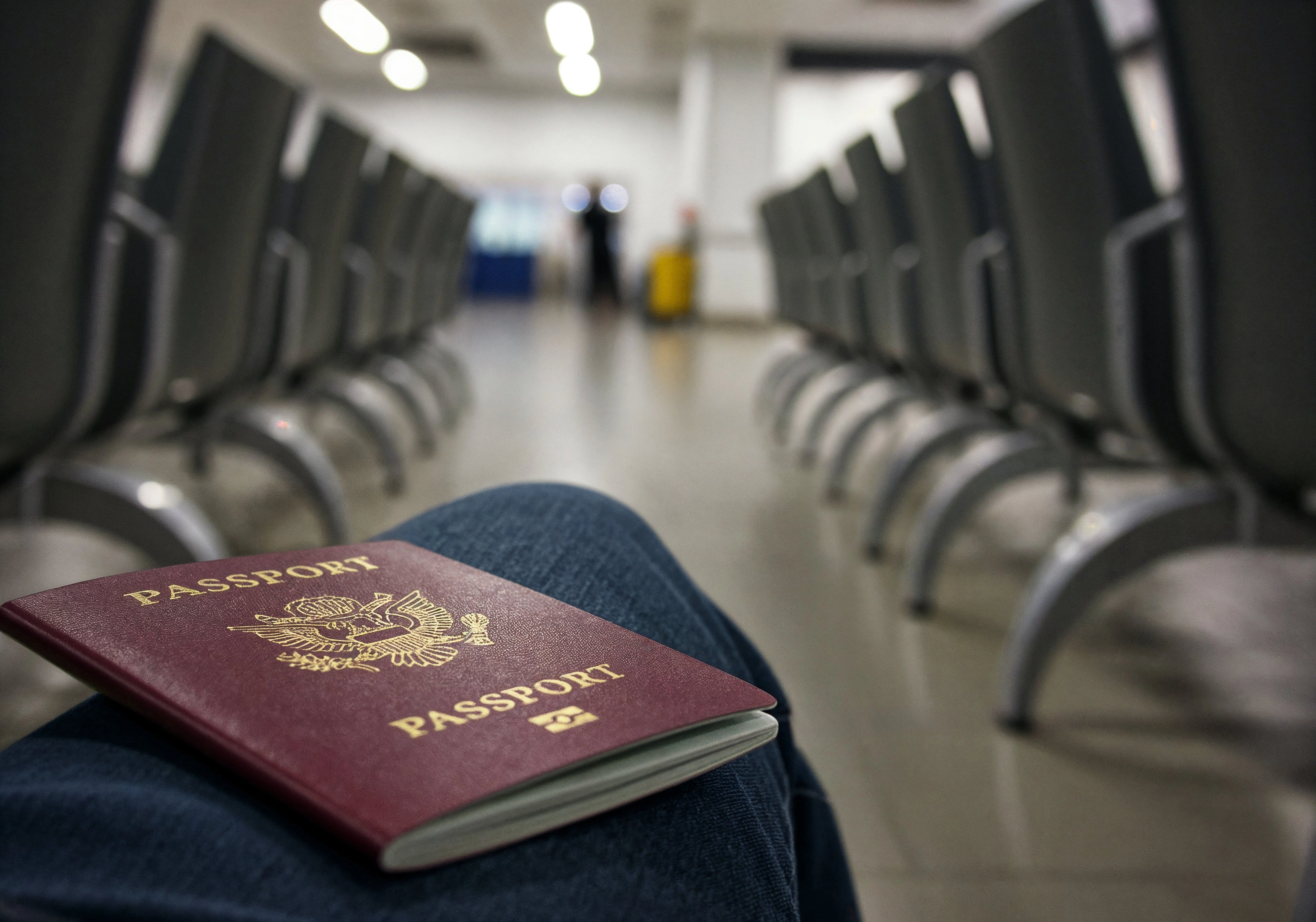 Pasaporte apoyado sobre la rodilla de una persona en una sala de espera vacía, que representa la incertidumbre que enfrentan los inmigrantes bajo el plan de deportación de Trump en 2025 y 2026